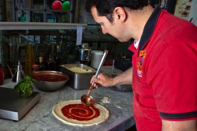 Pizzaiolo putting fresh sauce on pizza dough